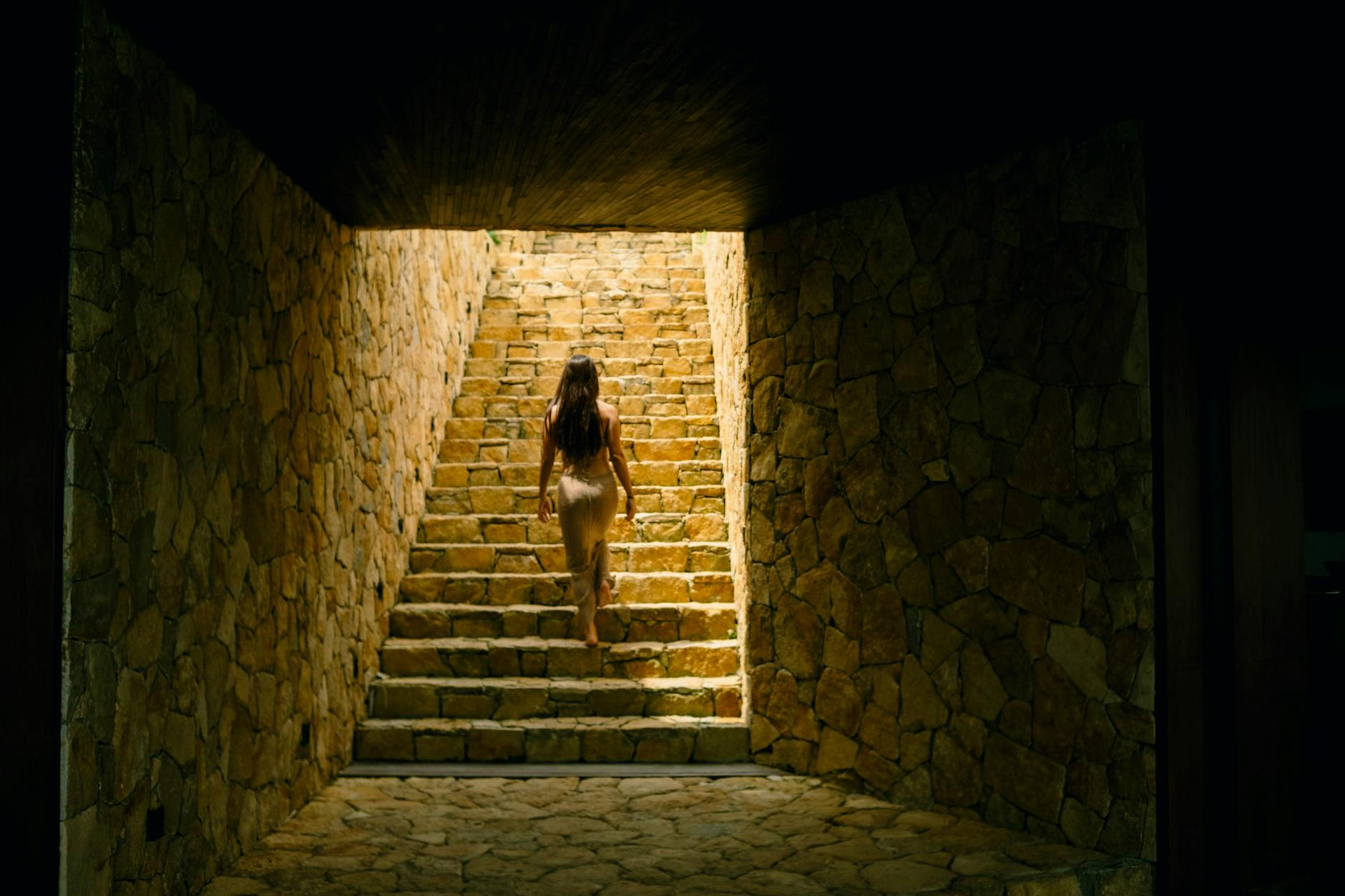 woman ascending stone staircase in rustic tunnel