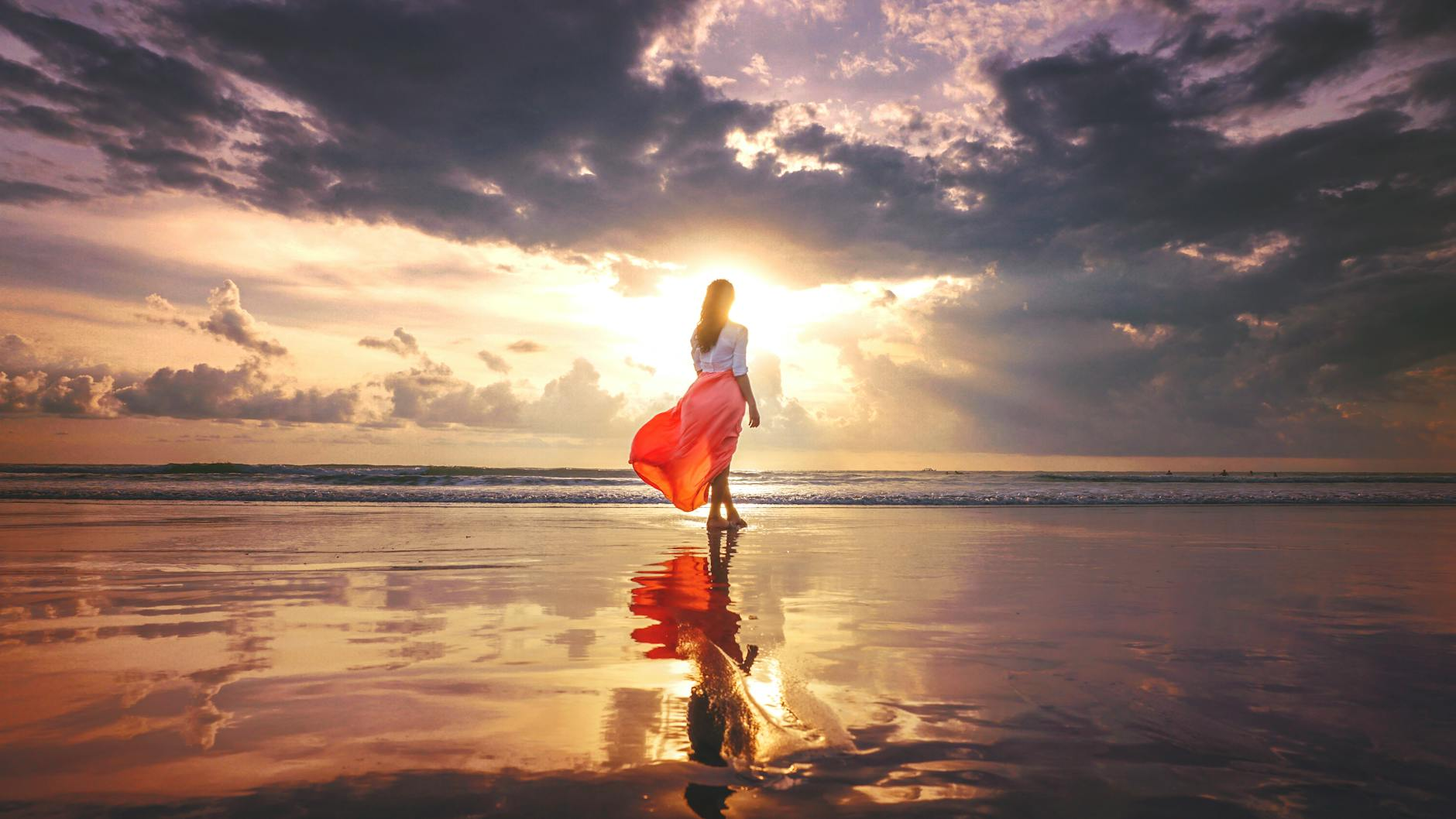 woman in a gauzy skirt standing on a beach at sunset