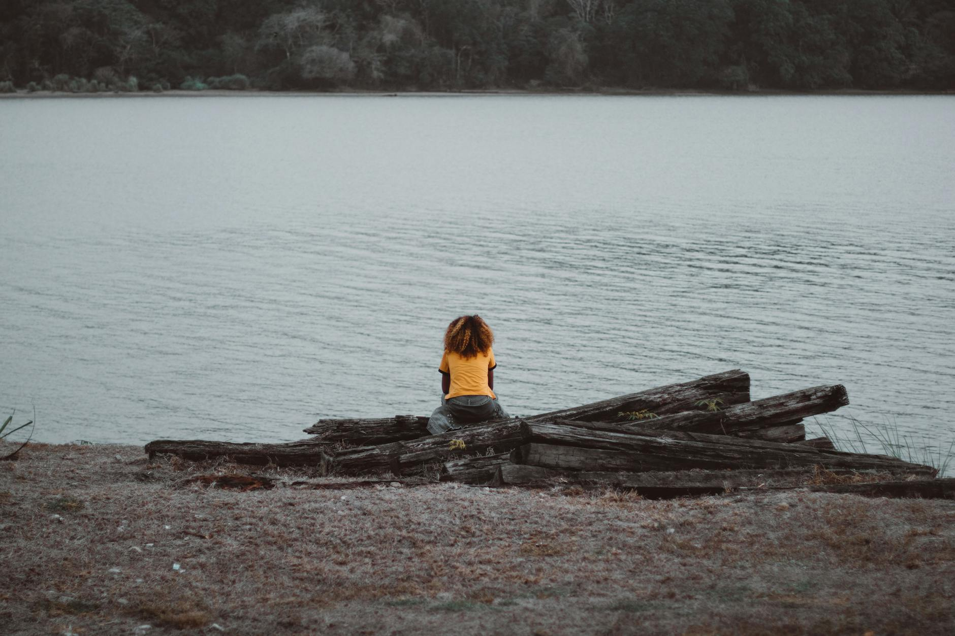 person wearing yellow shirt sitting near lake